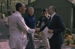 Sadat and Begin shake hands at Camp David while Jimmy and Rosalynn Carter look on